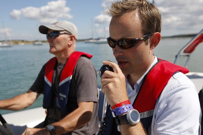 Two men both wearing lifejackets on a boat using a VHF radio to call for assistance. 
